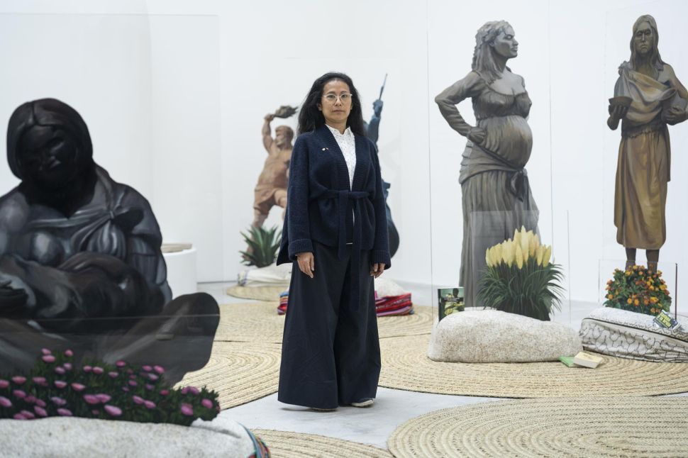 Discover The Unexpected Surge Of Contemporary Peruvian Art Woman standing in a gallery among sculptures and transparent panels with printed figures, with the text “Discover The Unexpected Surge Of Contemporary Peruvian Art” at the bottom