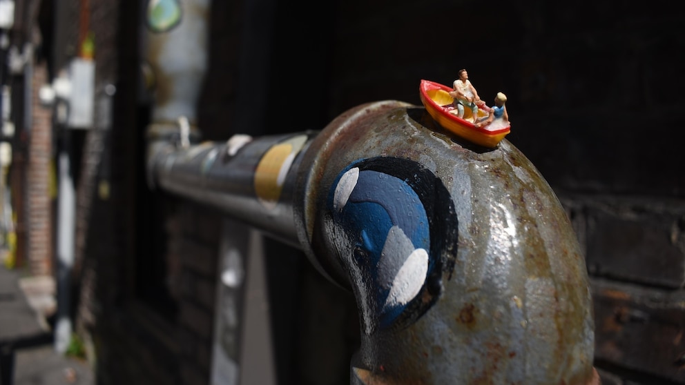 Step Inside: Mississippi’s Tiniest Museum Turns Alley Into Surrealist Wonderland 111 Miniature boat with tiny figures perched on a painted metal pipe in a narrow alley; visible text reads, “Step Inside: Mississippi's Tiniest Museum Turns Alley Into Surrealist Wonderland 111”